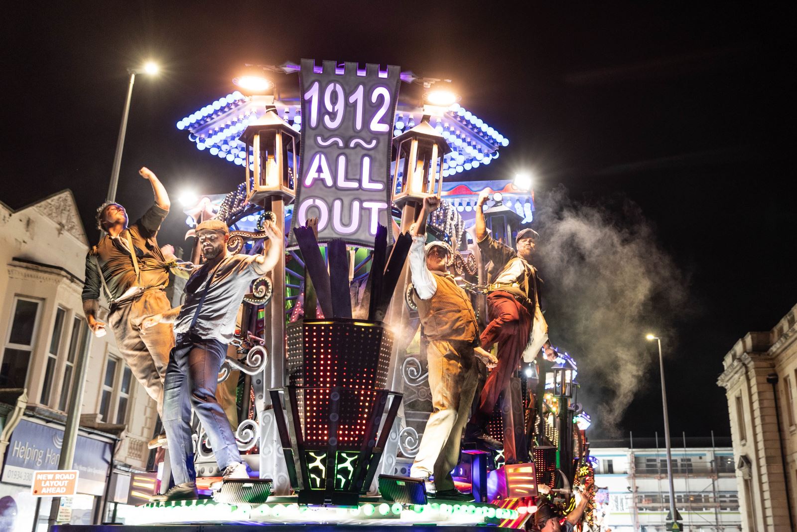 Four performers raise their fists in the air as they stand on top of a cart at the Weston-super-Mare Carnival commemorating the 1912 coal strikes